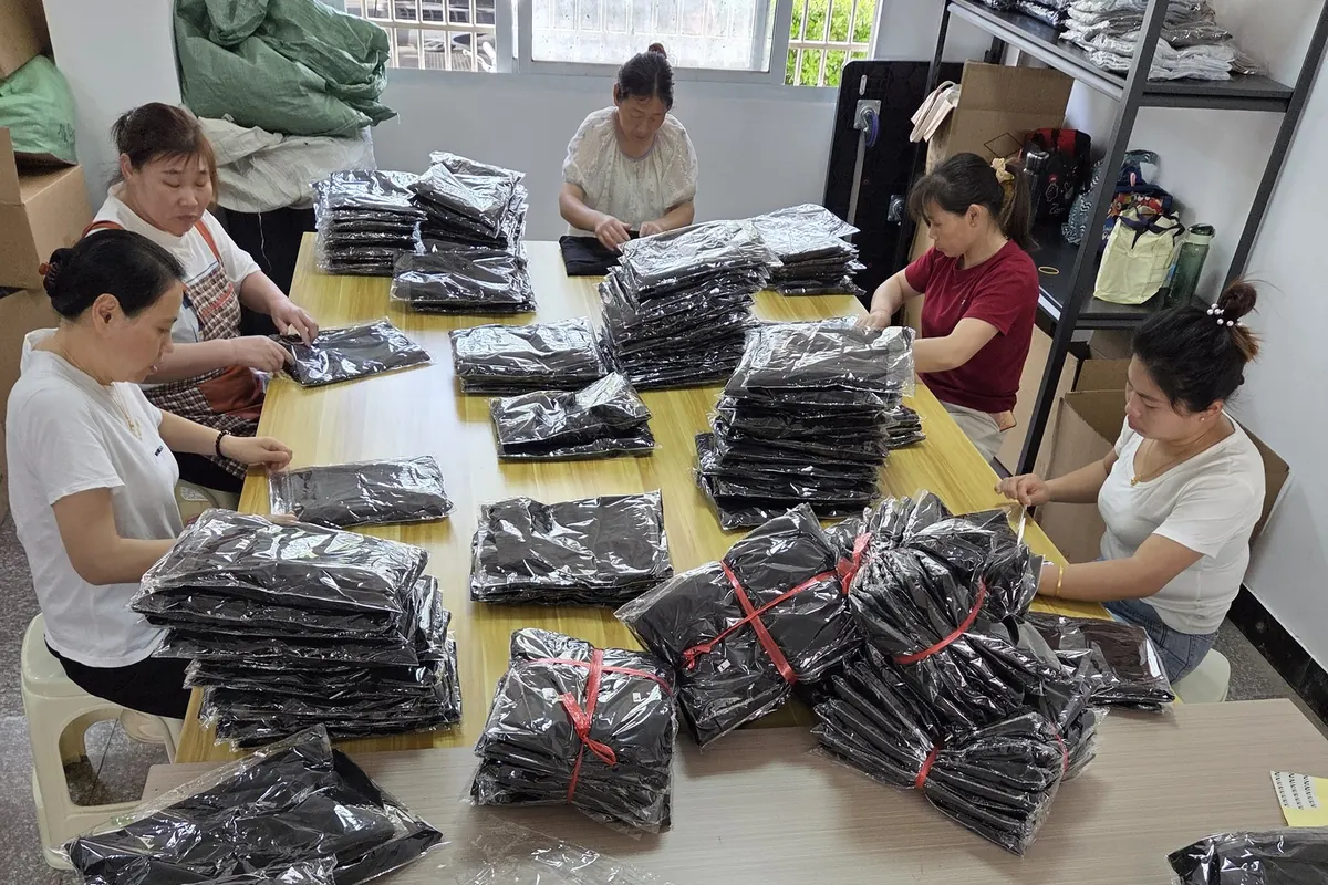 Staff around a table folding, bagging and banding finished garments before dispatch