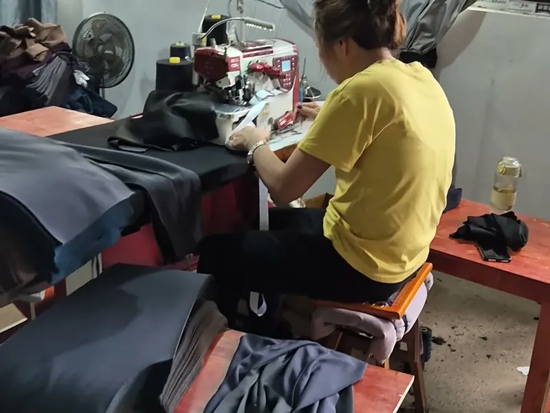 An operator working at a sewing station with cut panels stacked beside her