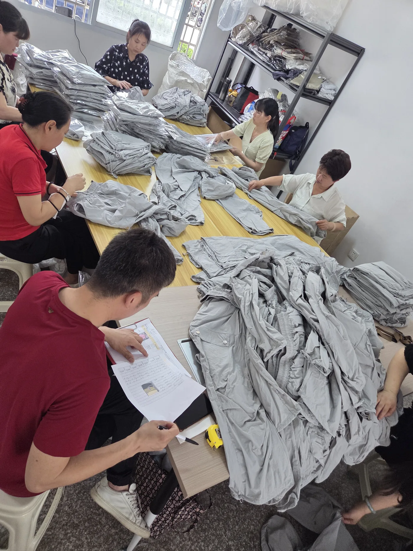 Groundwork staff checking a QC sheet and inspecting finished garments on the floor in China